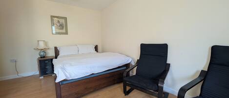 Un dormitorio con cama de madera, una mesita de noche, una lámpara, una silla y un cuadro colgado en la pared.