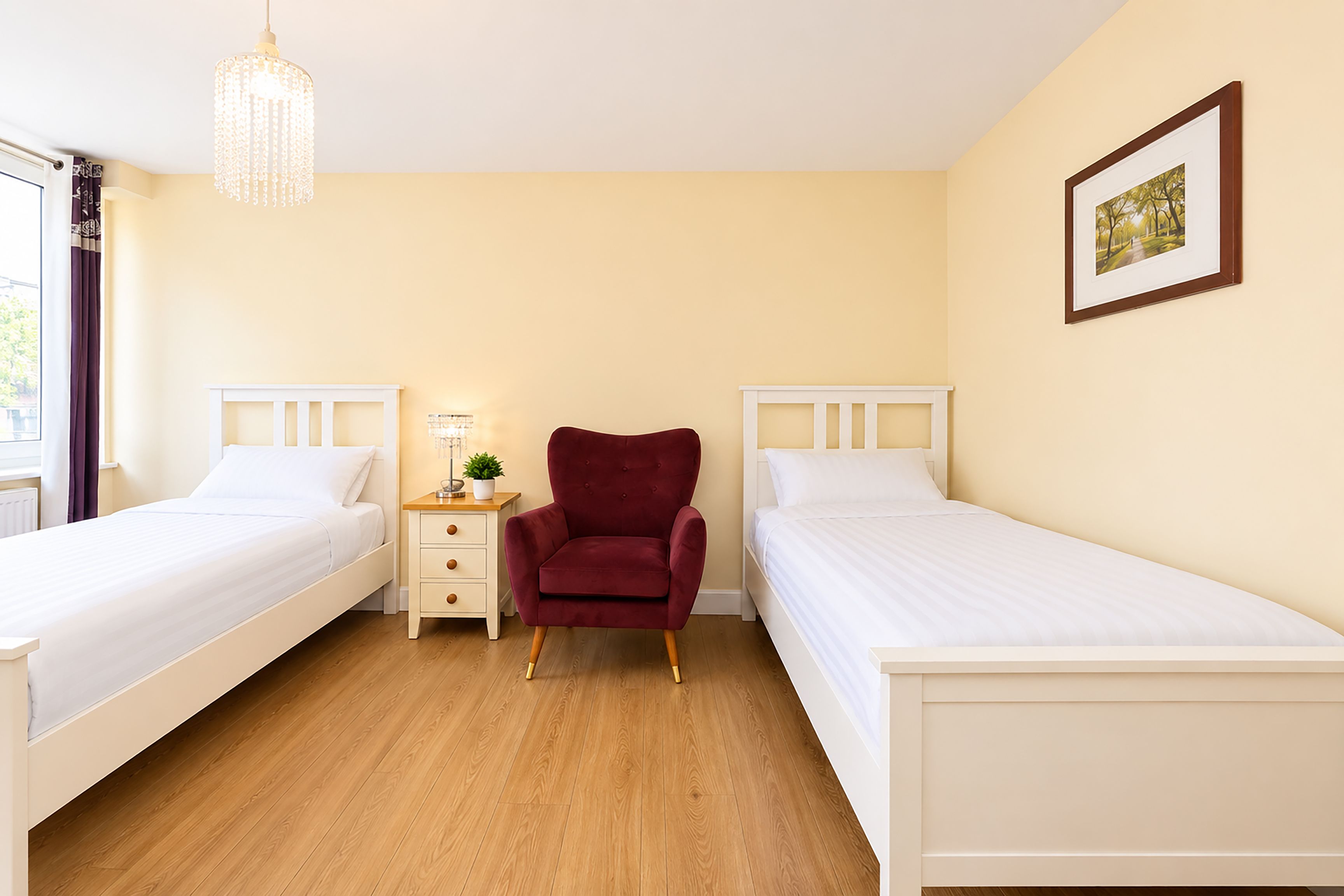 A hotel room with two single beds, a nightstand with a lamp, a red chair, and a framed picture on the wall.