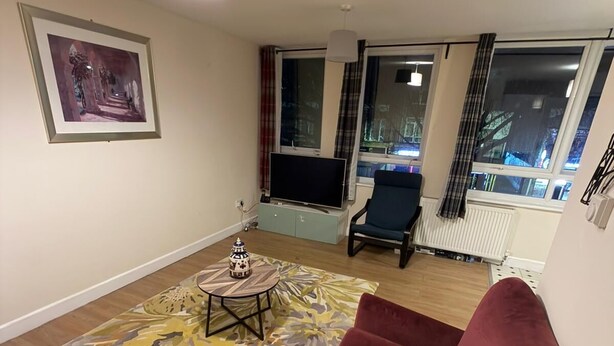 Een woonkamer met een bank, een rode fauteuil, een salontafel, een televisie en een schilderij aan de muur.