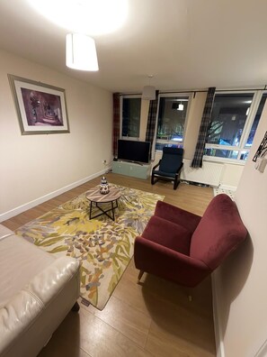 Una sala de estar con un sofá, un sillón rojo, una mesa de centro, un televisor y un cuadro en la pared.