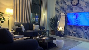 Ein modernes Wohnzimmer mit einem dunklen Sofa, einem Couchtisch, einem Fernseher und einem großen Fenster mit Vorhängen.