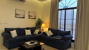 Ein Wohnzimmer mit einem dunkelblauen Sofagarnitur, einem Couchtisch mit Fernbedienung und einem Fenster mit Vorhängen.
