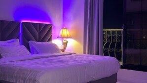 Ein Schlafzimmer mit einem Bett, einem Nachttisch, einer Lampe und Blick auf einen Balkon mit Geländer.