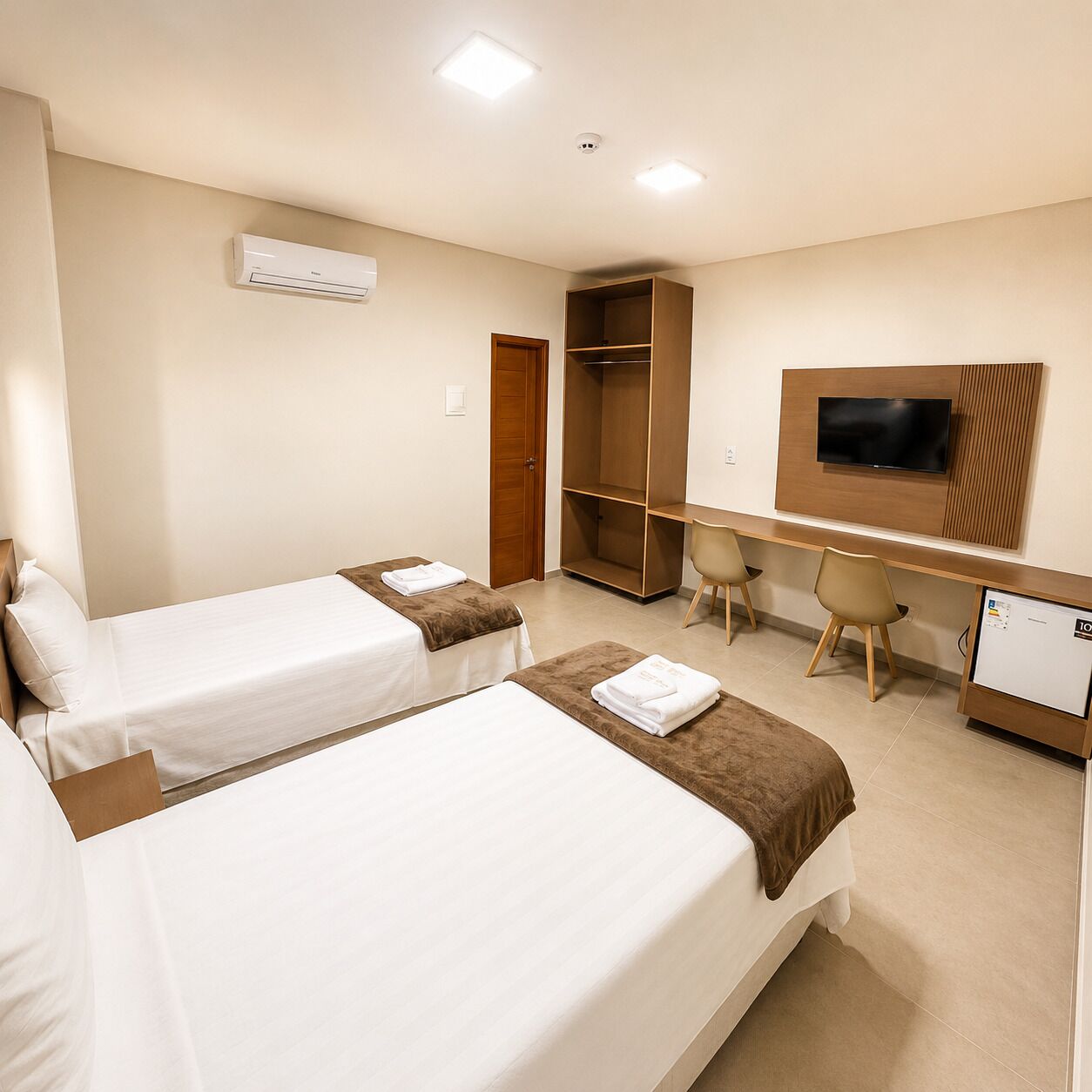 Habitación de hotel con dos camas, un escritorio con sillas, televisión y armario.