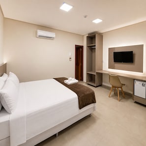 Una habitación de hotel con cama, escritorio, silla, televisor y armario.