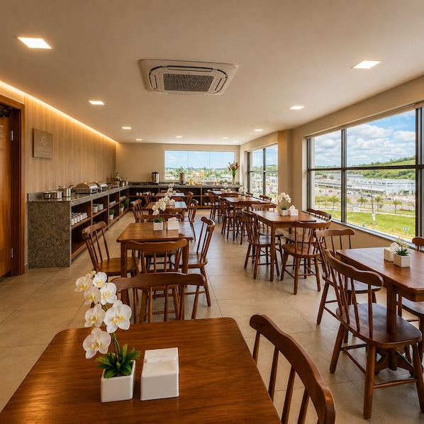 Un comedor amplio con múltiples mesas y sillas, una zona de cocina con disposición tipo bufé y grandes ventanales que ofrecen vistas al exterior.