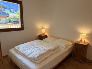 Ein Einzelbett mit Holz-Kopfteil, zwei Nachttische mit Lampen und ein Fenster mit Blick auf eine Berglandschaft.