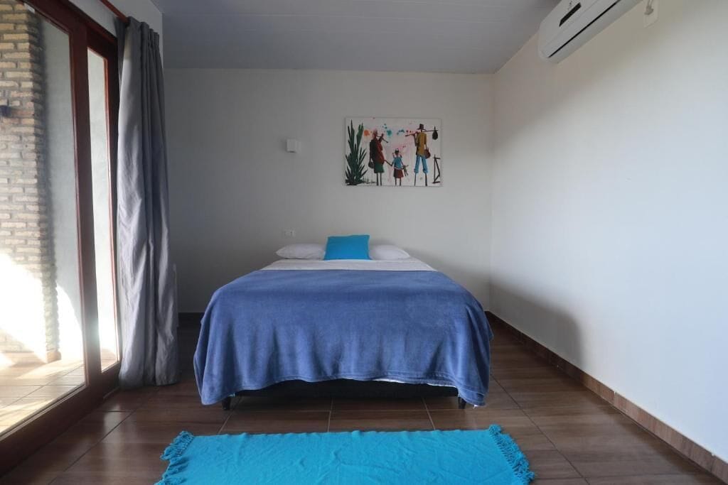 Ein Schlafzimmer mit Bett, einem Fenster mit Vorhängen, einer Wand-Klimaanlage und einem Bild an der Wand.
