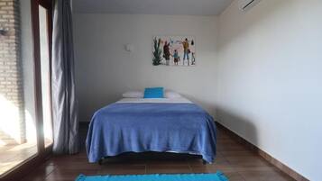 Ein Schlafzimmer mit Bett, einem Fenster mit Vorhängen, einer Wand-Klimaanlage und einem Bild an der Wand.