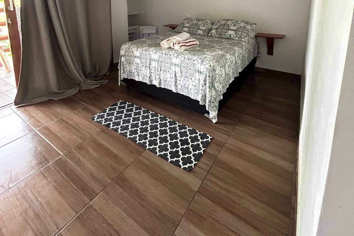 A bedroom with a bed, a patterned rug, a painting, and a ceiling fan.