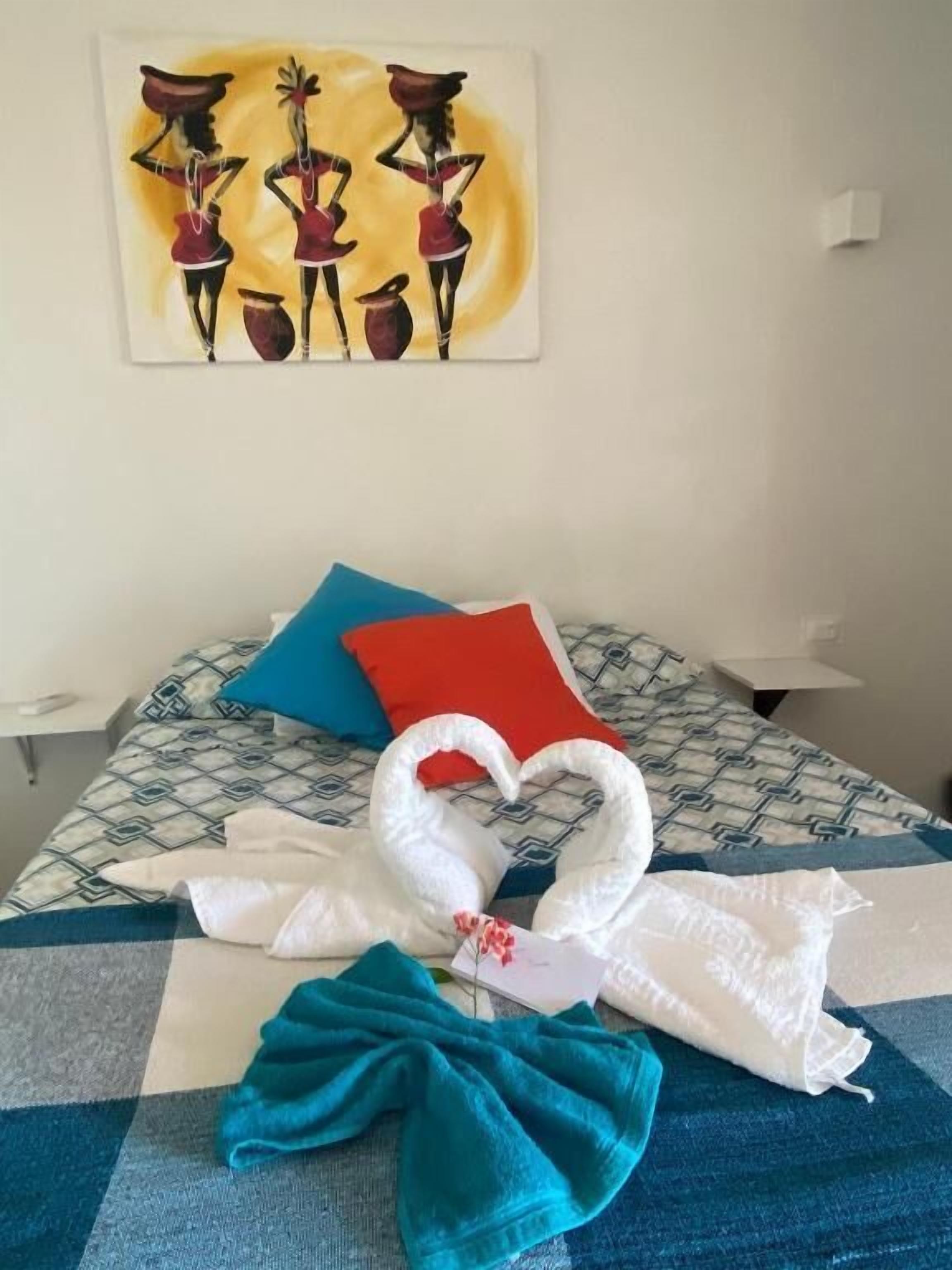 Ein Bett mit einem gemusterten Überwurf, zwei Kissen, ein herzförmiges Handtuch und ein Bild an der Wand.