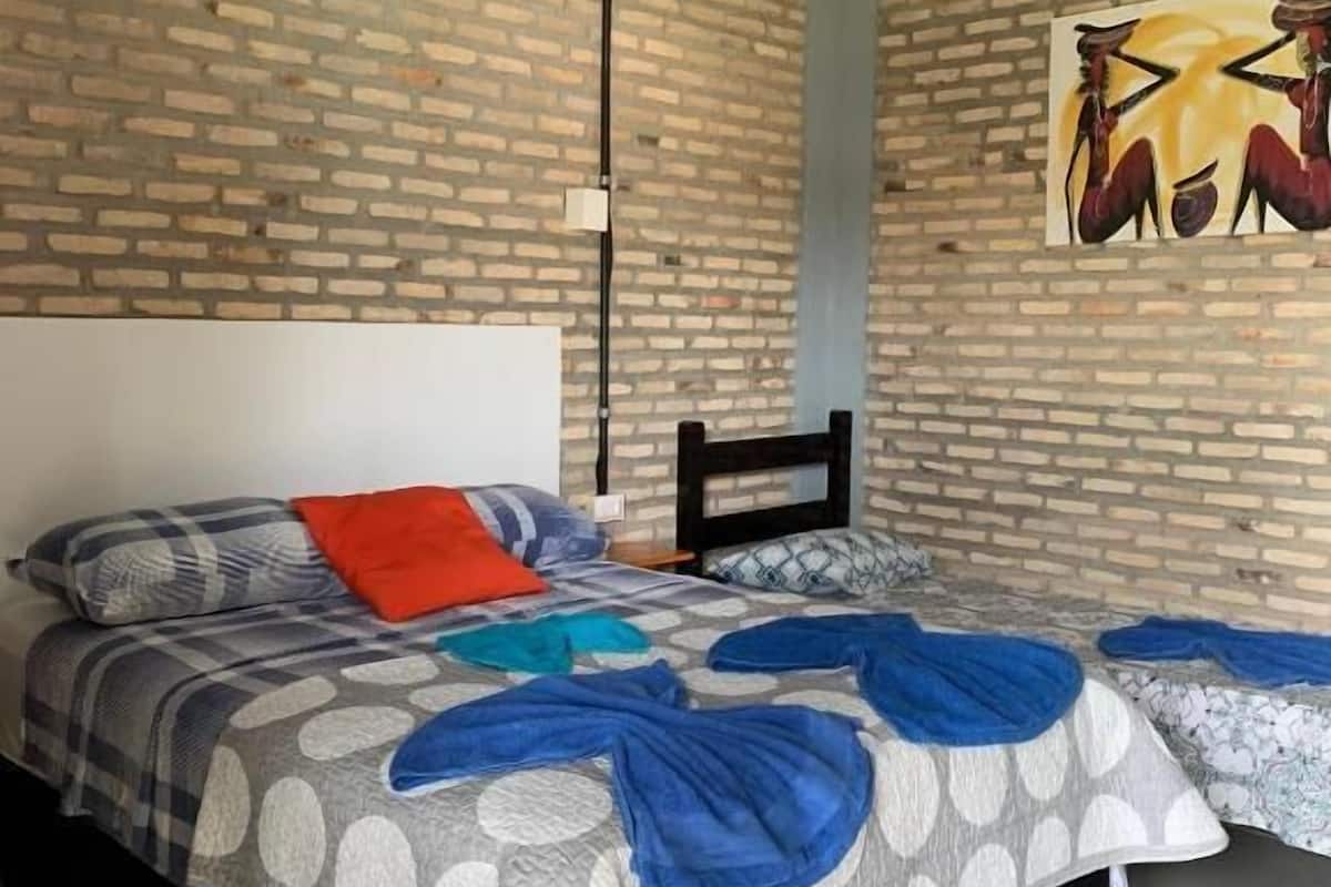 A bedroom with a brick-patterned wall, a bed with a polka dot and solid-colored duvet, a red pillow, and a painting of birds.