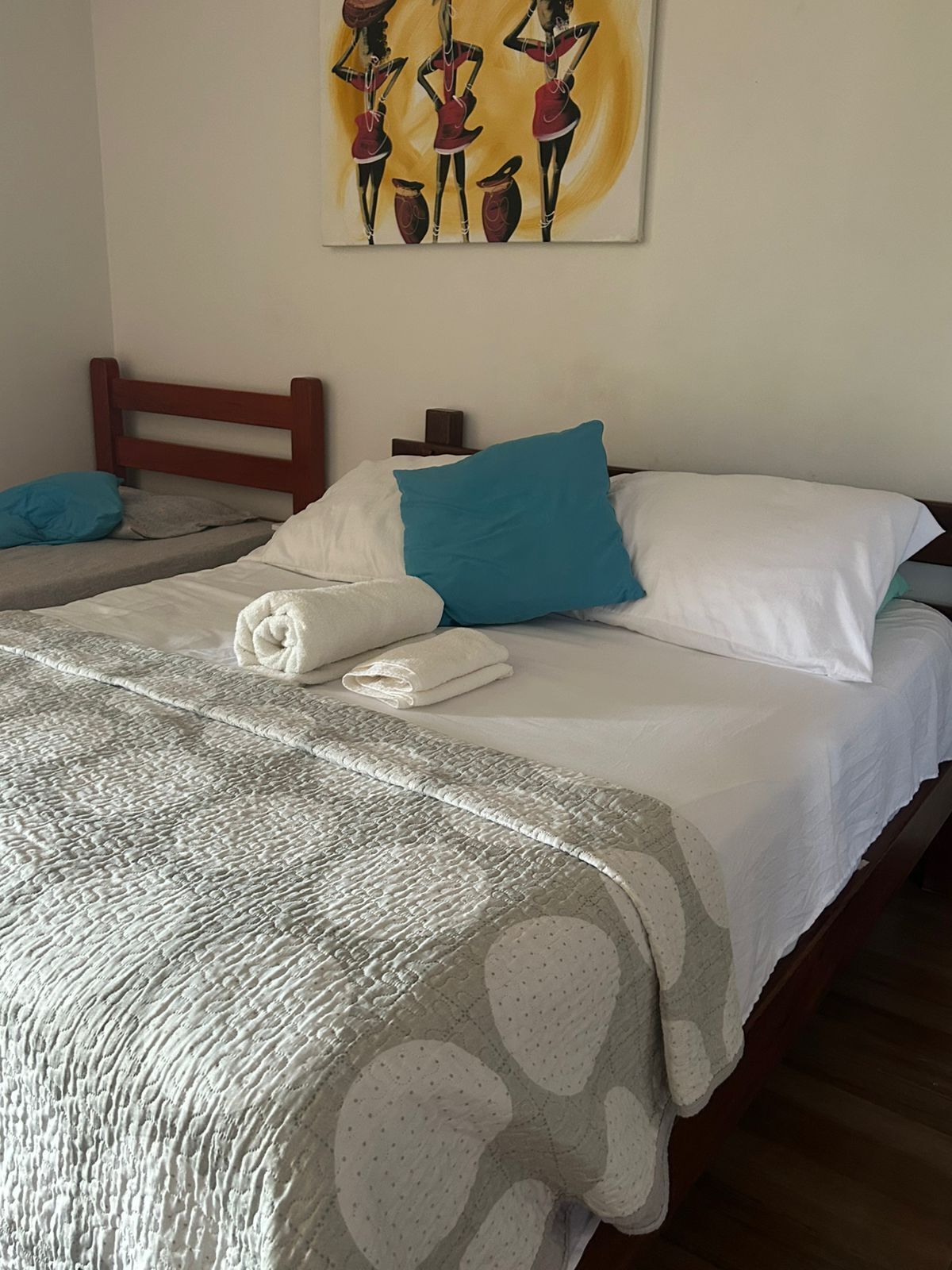 Une chambre d’hôtel avec deux lits, chacun agrémenté d’un oreiller blanc et bleu, d’une couverture grise à texture et d’un tableau au-dessus des lits.