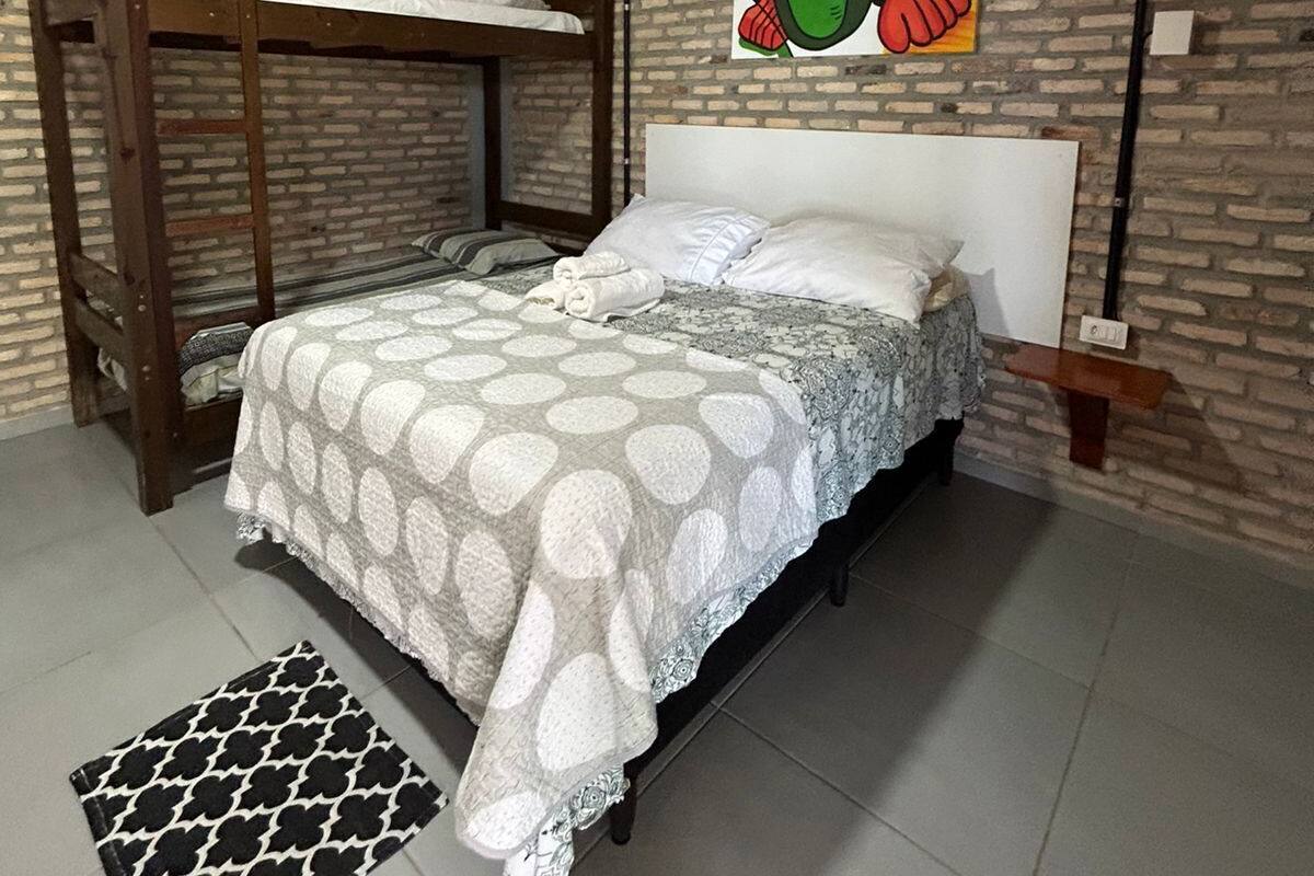 A bedroom with a bunk bed, a patterned bedspread, a decorative wall hanging, and a small bedside table.