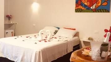 A neatly made bed with a white bedspread, a bouquet of roses, and a heart-shaped decoration on the headboard. A colorful abstract painting adorns the wall above the bed.