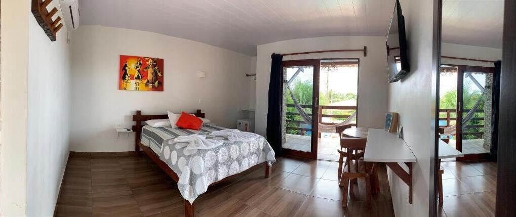 Een slaapkamer met een bed, een bureau en een stoel. Er hangt een schilderij aan de muur en er is een raam met uitzicht op groen.