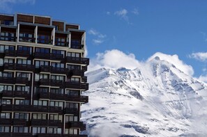 Um hotel com vários andares e varandas, com uma paisagem de montanha coberta de neve ao fundo.
