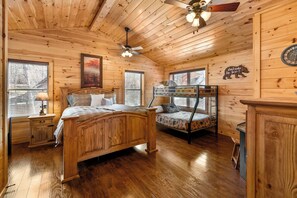 A wooden cabin bedroom with a bed, bunk bed, and a ceiling fan. - Charming Chalet Getaway in Prime Location, with Hot Tub & Pools (Pigeon Forge)