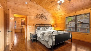 Ein Schlafzimmer einer Holzhütte mit einem Bett, Nachttischen und einem Fenster mit Blick auf ein Haus.