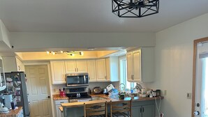 A spacious kitchen with white cabinets, a wooden dining table, and a central island. - Views for Days! Flathead Lake Retreat 1 mile to Downtown (Polson)
