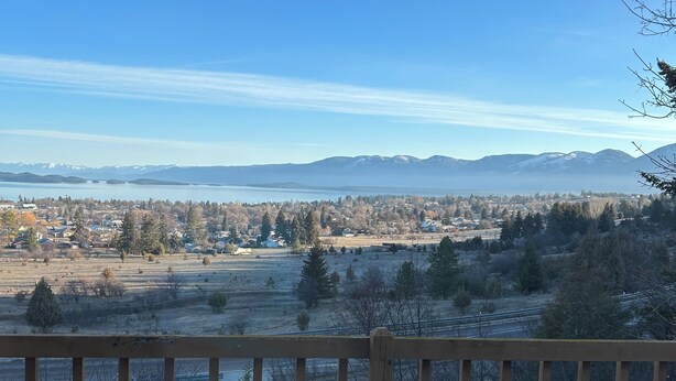 A wooden deck with a table and chairs, overlooking a town and mountains. - Views for Days! Flathead Lake Retreat 1 mile to Downtown (Polson)