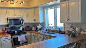 A modern kitchen with white cabinets, a built-in microwave, a large island with bar stools, and a window providing natural light. - Views for Days! Flathead Lake Retreat 1 mile to Downtown (Polson)