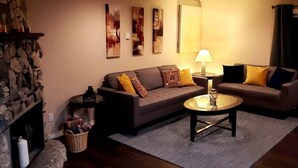 A cozy living room with a stone fireplace, a sofa set, a coffee table, and wall art. - MALASPINA HIDEAWAY 2 (Powell River)