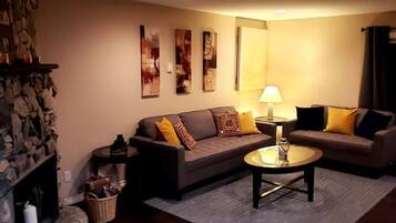 A cozy living room with a stone fireplace, a sofa set, a coffee table, and wall art.