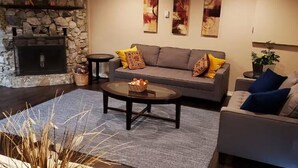 A cozy living room with a stone fireplace, a grey sofa with yellow cushions, a round coffee table, and a grey armchair. - MALASPINA HIDEAWAY 2 (Powell River)