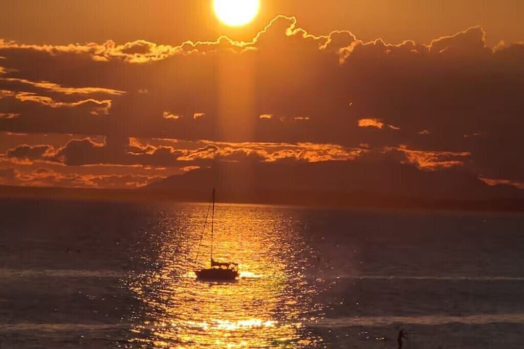 A sunset over a body of water with a sailboat.