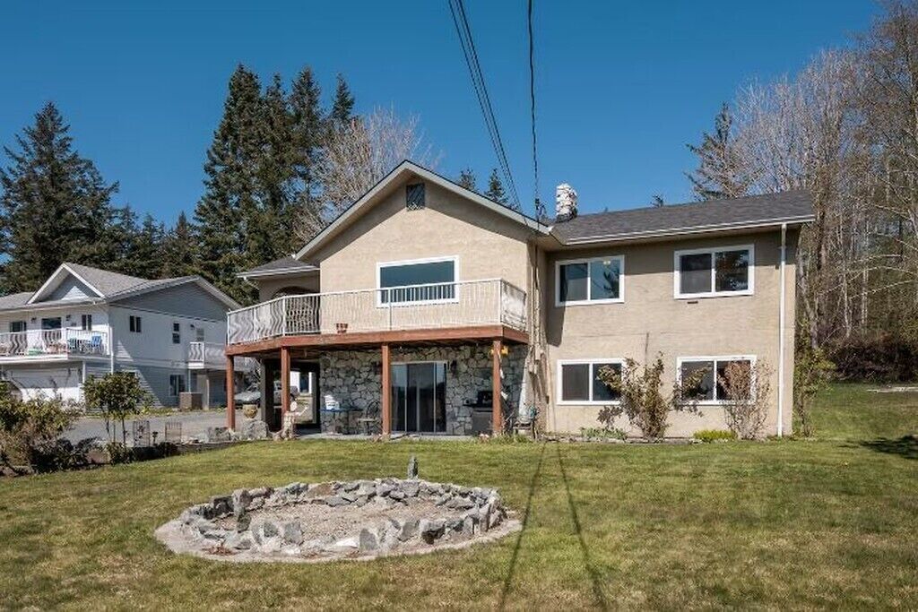 A two-story house with a balcony, stone foundation, and a stone fire pit in the yard.