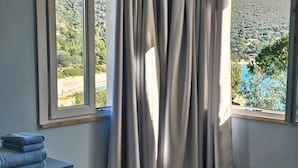 A bedroom with a bed, a window with curtains, a dresser, and a view of a landscape. - Villa Serena by the sea (MARACALAGONIS)