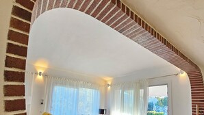A modern living room with a brick staircase, a yellow sofa, red armchairs, and a dining area with a view. - Villa Serena by the sea (MARACALAGONIS)