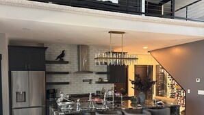 A modern kitchen with a central island, bar stools, and a chandelier.