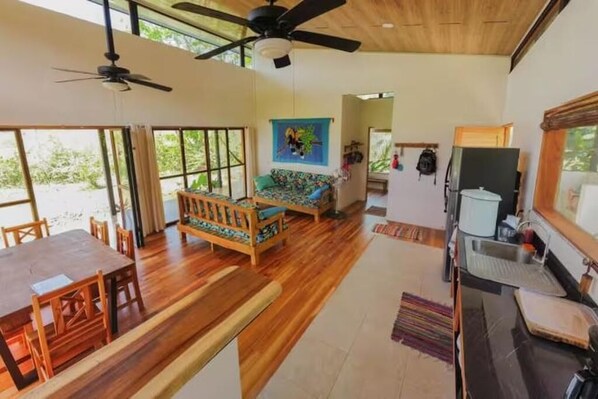 A spacious living area with a wooden floor, a sofa, a dining table, and a ceiling fan. - Jungle Bungalow in Drake Bay (Puntarenas Province)