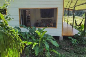 A small, single-story house with a large window and a hammock outside. - Jungle Bungalow in Drake Bay (Puntarenas Province)