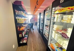 Ein Korridor mit Regalen an beiden Seiten, eine Person in der Ferne und ein Kühlschrank mit verschiedenen Gegenständen.