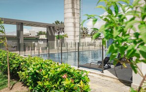 A swimming pool with a glass barrier, lounge chairs, and a concrete pillar. - 1503 Apto 2 Qtos completo João Pessoa (Cabedelo)