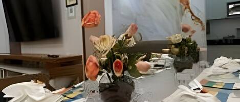 A dining table set with plates, cutlery, and a vase with flowers.