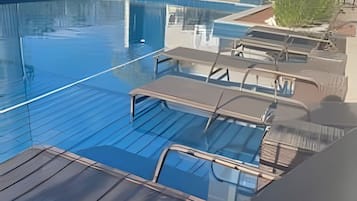Uma piscina com espreguiçadeiras e barreira de vidro.