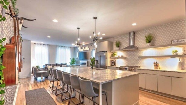 Uma cozinha moderna com uma ilha central, banquetas, fogão embutido e luminária pendente.