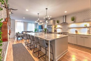 A modern kitchen with a central island, bar stools, a built-in stove, and a hanging light fixture. - 2 Homes | Double Rooftop | 360° DT Views | 24 beds (Nashville)