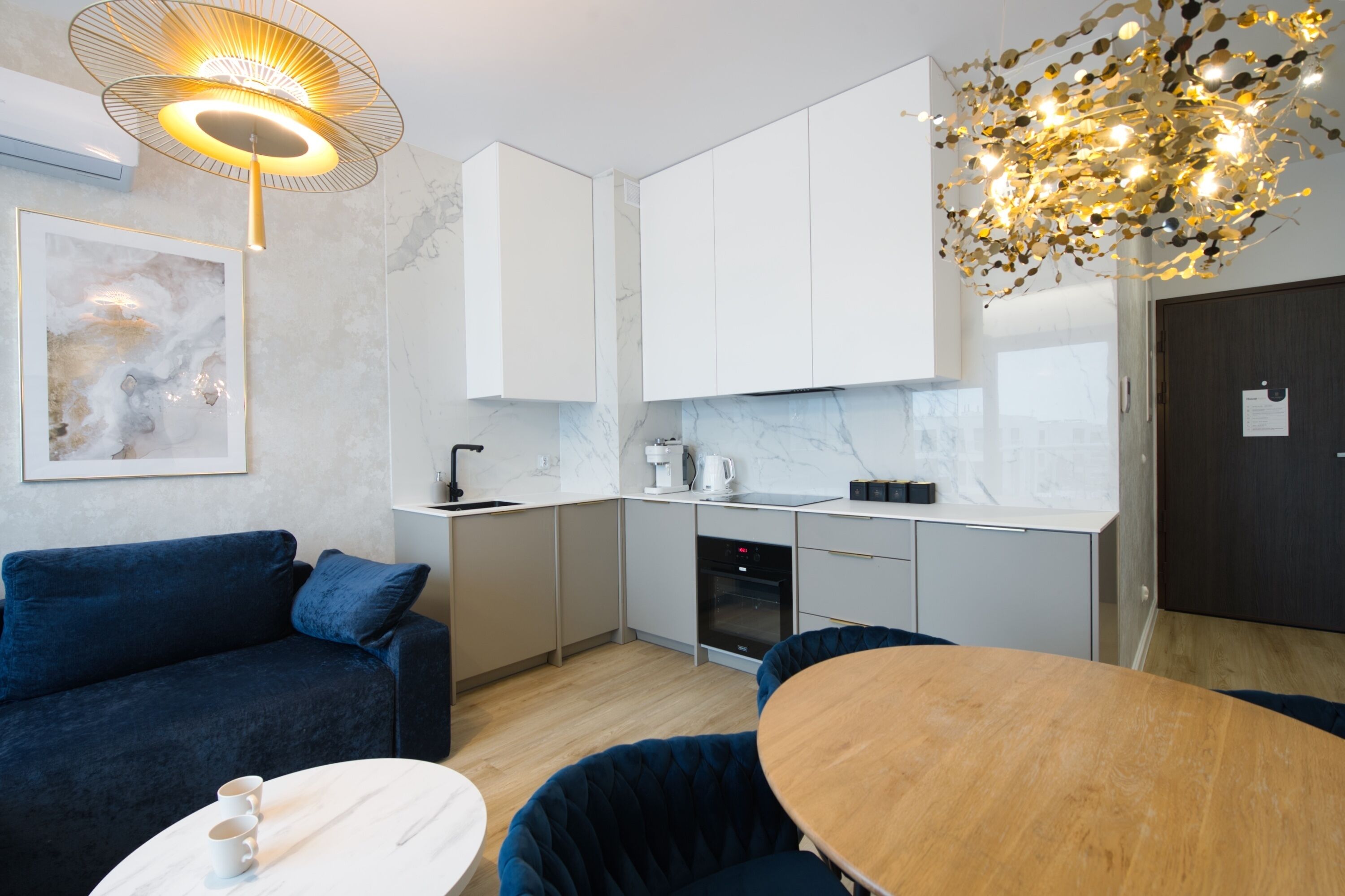Una cocina moderna con gabinetes blancos, salpicadero de mármol y un área de comedor con mesa redonda y sillas azules.