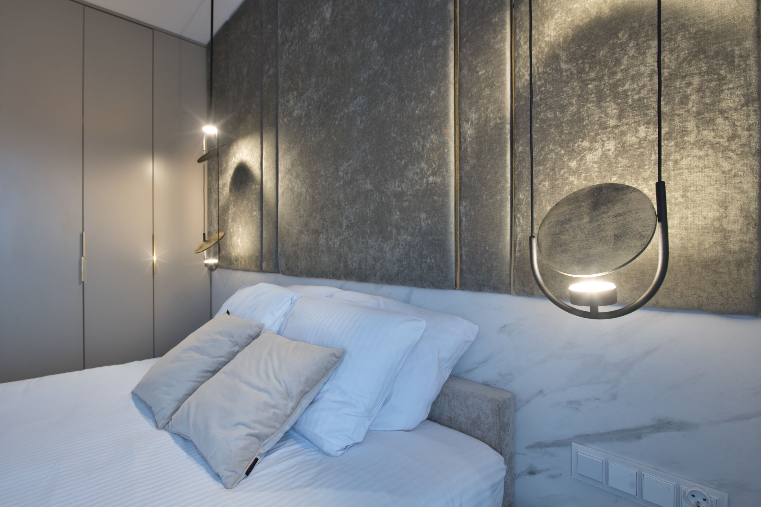 A modern bedroom with a bed, white bedding, a marble headboard, and wall-mounted lighting.