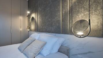 A modern bedroom with a bed, white bedding, a marble headboard, and wall-mounted lighting.