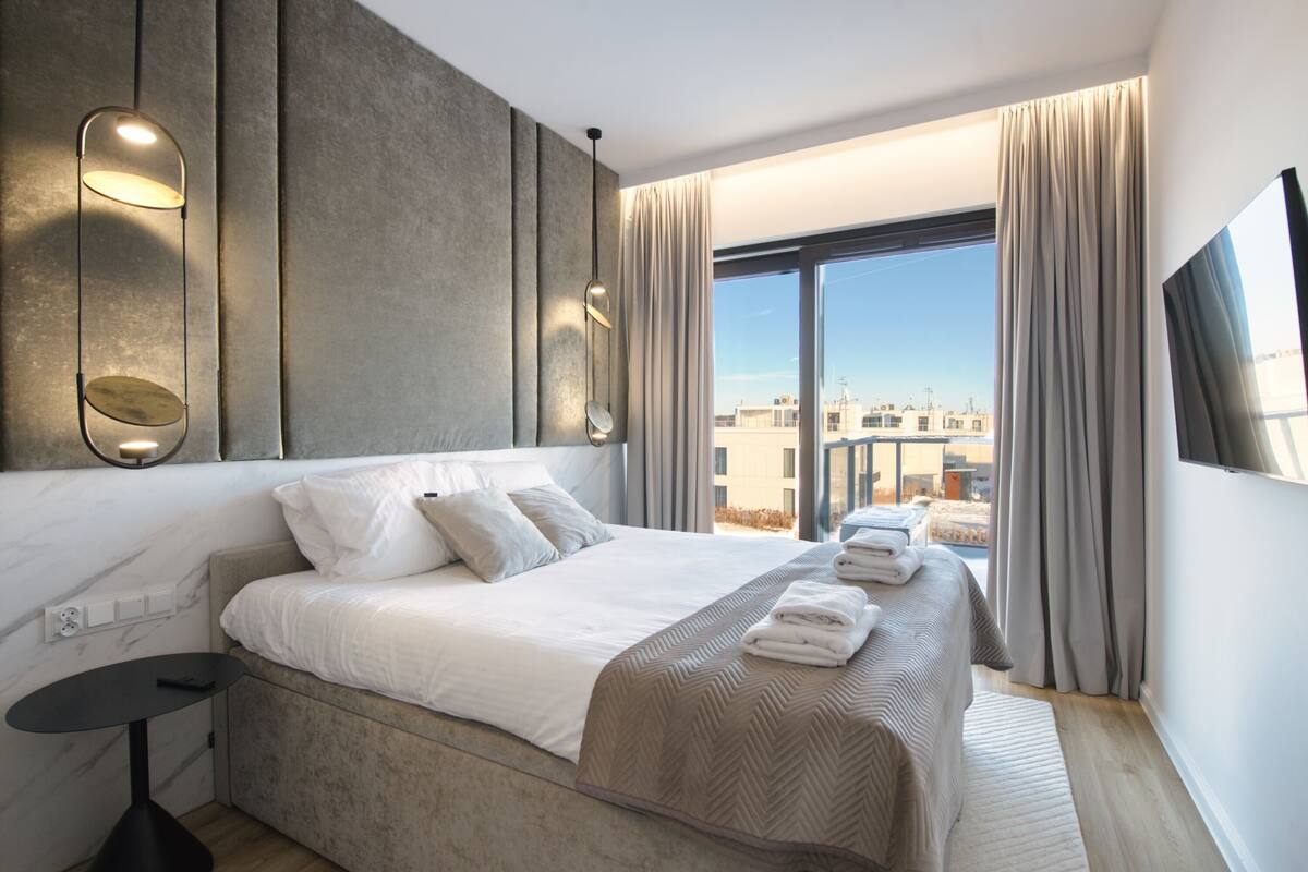 A modern hotel room with a large bed, a view of the city, and a flat-screen TV.