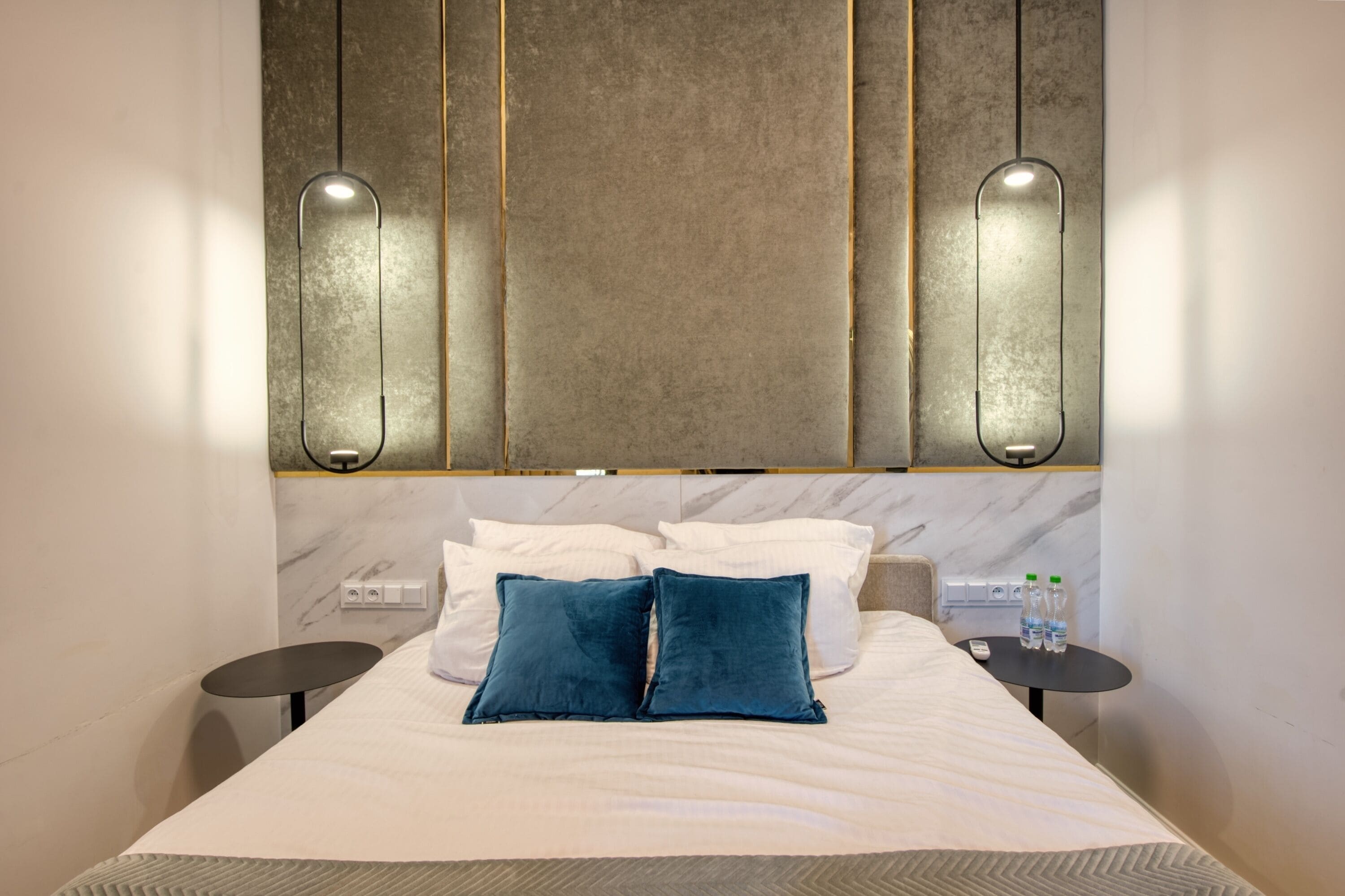 Une chambre d’hôtel avec un lit, deux tables de chevet, une tête de lit en marbre et des lampes fixées au mur.