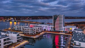 Un hotel frente al agua con arquitectura moderna, un puerto deportivo y un río.