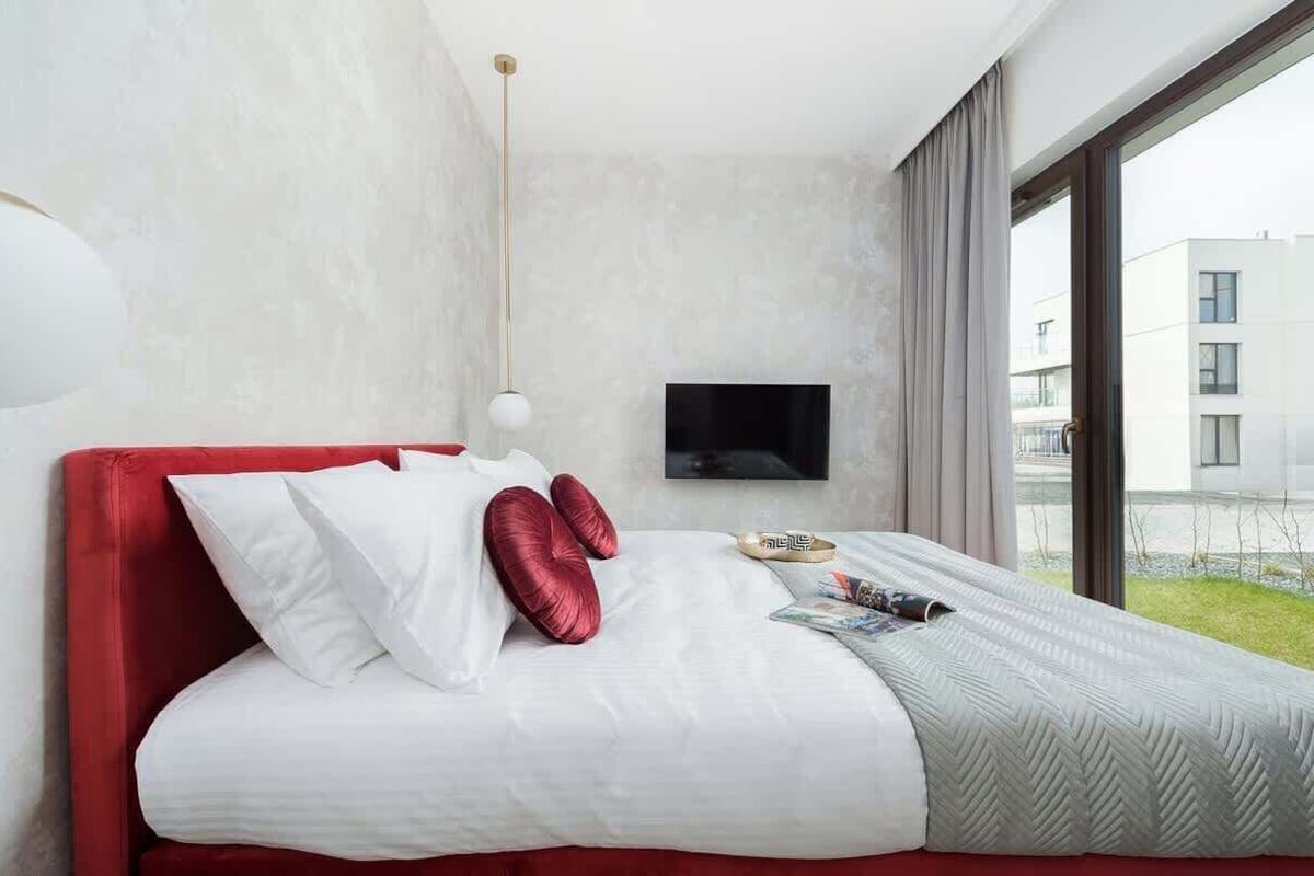 A modern hotel room with a large bed, a flat-screen TV mounted on the wall, and a view of the outside building through the window.