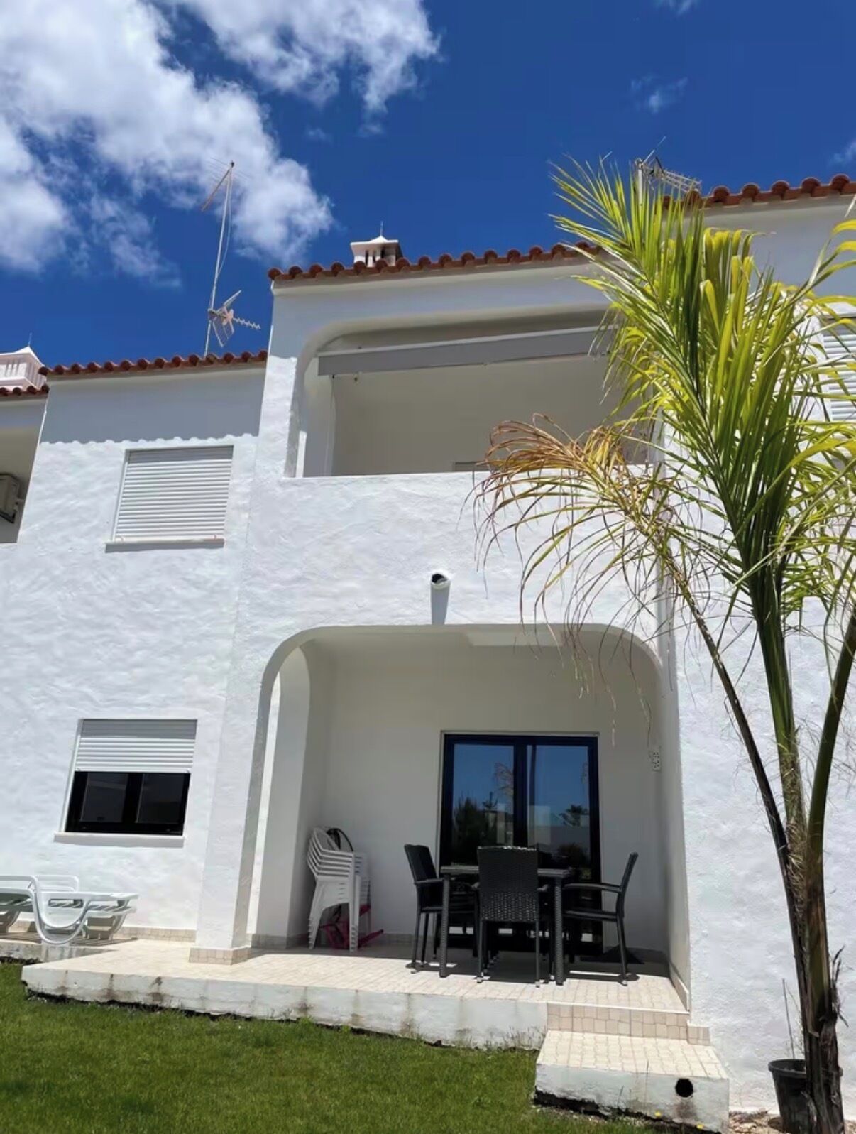 A two-story building with a white exterior, a balcony, and a small patio area with outdoor furniture.